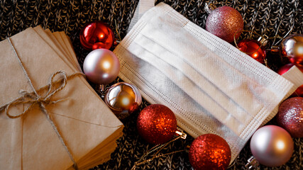 Christmas envelopes with a medical mask and red and pink balls on a knitted background