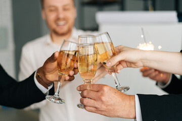 Close-up view of business team of multinational employees holding clinking glasses of champagne and smiling cheerfully at corporate New Year or Happy Christmas eve.