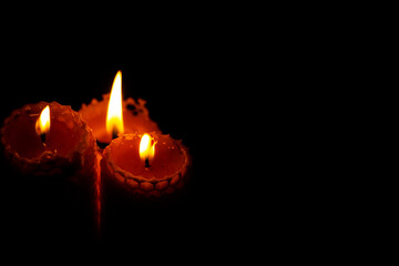Close-up of three small yellow candles on a black background.