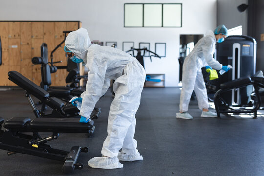 Team Of Workers Wearing Protective Clothes And Face Masks Cleaning The Gym Using Disinfectant