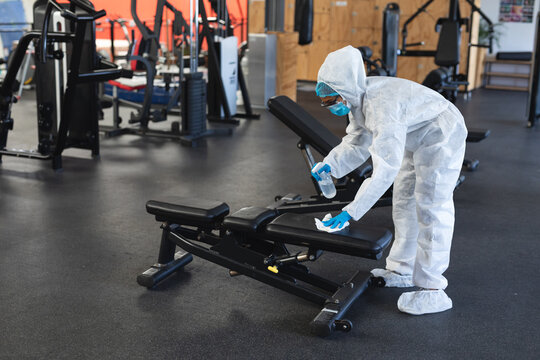 Female worker wearing protective clothes and face masks cleaning the gym using disinfectant