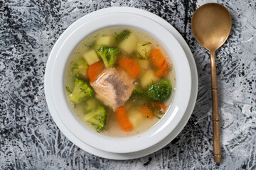Fresh salmon fish soup with carrots, potatoes and onions in a white plate, close up. Top view