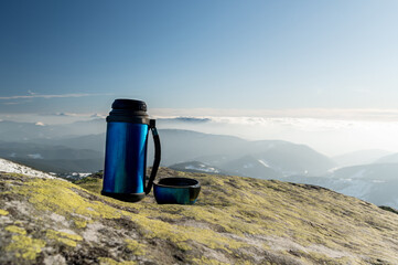 Thermos for drinks on a background of mountains. Thermos on a stone outdoors.