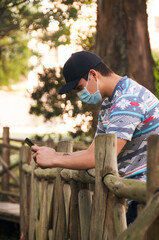 Young man  wearing a medical mask using his cell phone in the forest 