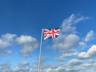 UK union jack flag blowing in the wind  against blue cloudy sky background with copy space 