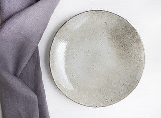 Gray linen towel and ceramic plate on a white wooden background. Serving.