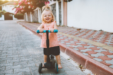 Child girl riding scooter on city street happy baby 1 year old healthy active lifestyle family fun outdoor © EVERST