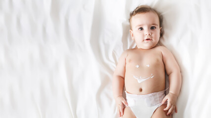 Funny little kid wearing in diaper. Portrait of a cute baby 6 months old lying on a white blanket. Smile sign on a baby's belly painted with a cream. Looking at the camera