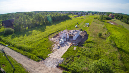 Aerial view on detached house under construction. House in basic state. Located on green plot in small village. building materials around. Meadows around.