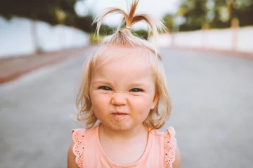 Fototapeten Child girl smiling face portrait cute baby 1 year old candid emotions blond hair funny kid looking at camera close up outside © EVERST