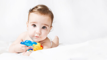 Cute funny baby girl in diaper playing with rattle on white bed in your room. portrait toddler. Looking at the camera. copy space