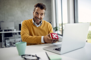 Happy businessman showing a present while talking to someone over laptop in the office.