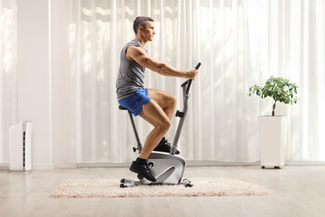 Fit muscular man in sportswear riding a stationary bike at home