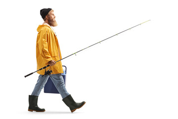 Full length profile shot of a bearded fisherman walking and carrying a fridge and a fishing rod