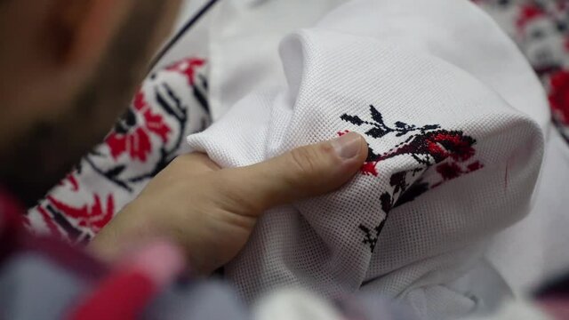 A man does the cross-stitch the wedding towel with a red thread. Close-up shot.