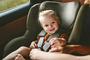 Child in a car girl in safety seat and mother fastens belt family lifestyle vacation with baby security transportation