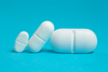 Three white  pills of different sizes on blue, dosage