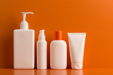 Still life with a set of white unbranded cosmetic bottles on orange background