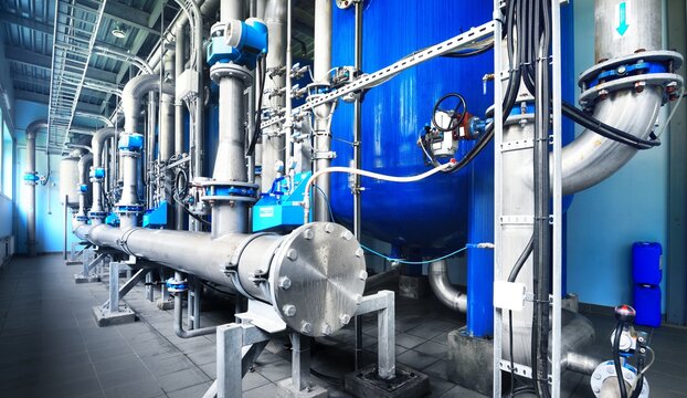 Large industrial water treatment and boiler room. Shiny steel metal pipes and blue pupms and valves.