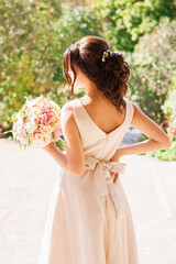 Portrait of merciful bride standing with wedding bouquet. Brunette at photoshoot in park