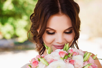 Portrait of merciful bride standing with wedding bouquet. Brunette at photoshoot in park