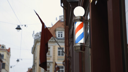 Bright red white blue barbershop pole on wall with ,  flag in background