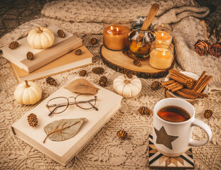 A table set for one with coffee or some magical elixir, on a knitted table cloth, with books to read and seasonal decorations that include small white pumpkins, pine cones and bright scented candles