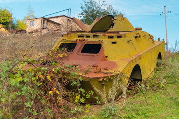 Side of an abandoned war tank with vegetation growing inside and some buildings in the backgrownd,...