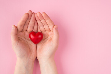 St. Valentine's day concept. Top above overhead pov first person view photo of female hands holding a red heart to the left side isolated on pink pastel background with copyspace