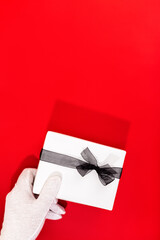 Santa Claus with gloved hands holding a Christmas Present on red background