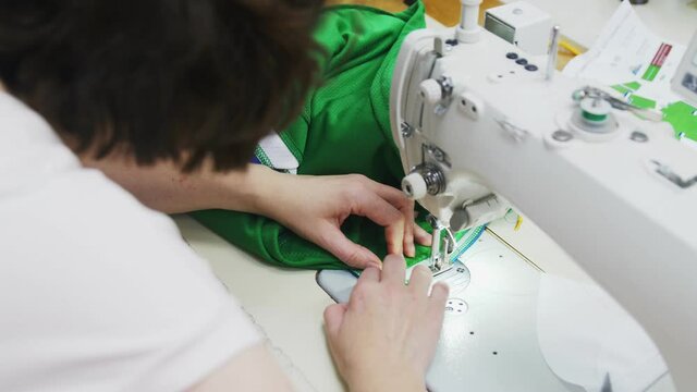 Seamstress makes serging seam on edge of fabric with machine