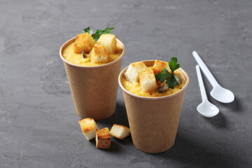 Pumpkin cream soup with croutons and pumpkin seeds in cups of craft paper on gray background. Soup...