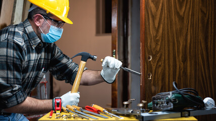 Carpenter worker at work repair and install a room door lock, wear the surgical mask to prevent...