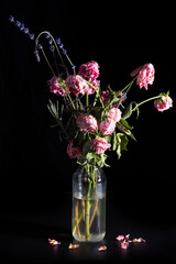 Wilted red roses in a glass vase on a dark background.