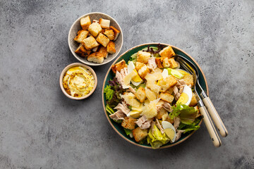 Fresh Caesar salad with lettuce salad, chicken breast, boiled eggs and croutons in ceramic bowl with dressing on the side on white table. Top view, healthy salad great for lunch, snack or appetizer