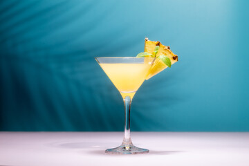 Refreshing pineapple cocktail with slice of pineapple and mint in front of shadow of palm leaves in a shining sun.