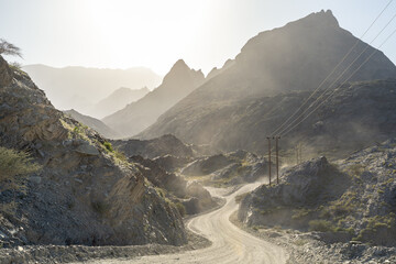 Winding mountain road descending through rocky desert canyon in Oman, illuminated by hazy sunlight