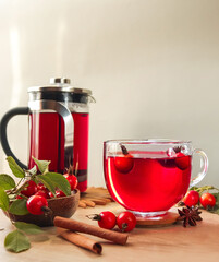 Teapot and glass cup with rosehip tea and hibiscus, next to a bowl with berries on a wooden table