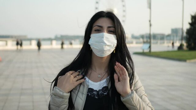 brunette Girl in mask in outdoor look to the mobile phone and wear the mask