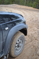 a big black SUV car is driving through the forest on a bad sandy road