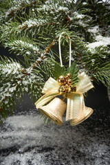Christmas decoration with bells, a branch of a Christmas tree and artificial snow on a black background.