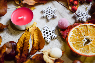 Sweet November. Candle on linen fabric with autumn leaves, decorative snowflakes, dried oranges and different decor. Selective Focus, top view, flat lay. Hugge concept with copy space.