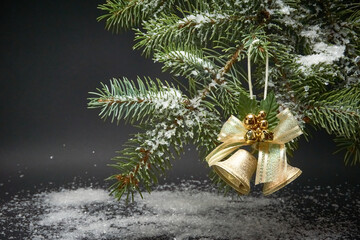 Christmas decoration with bells, a branch of a Christmas tree and artificial snow on a black background.