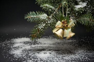 Christmas decoration with bells, a branch of a Christmas tree and artificial snow on a black background.