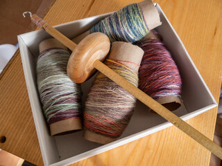 thread of spun wool wrapped around cardboard bobbins and wooden spindle