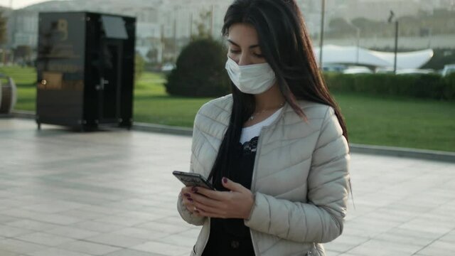 brunette Girl in mask in outdoor look to the mobile phone and wear the mask