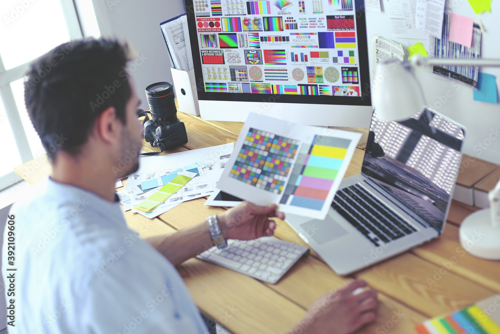 Poster portrait of young designer sitting at graphic studio in front of laptop and computer while working o