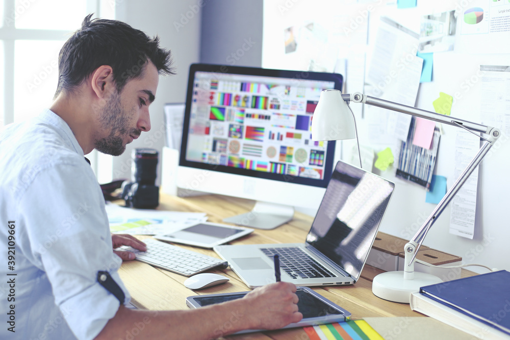 Poster portrait of young designer sitting at graphic studio in front of laptop and computer while working o