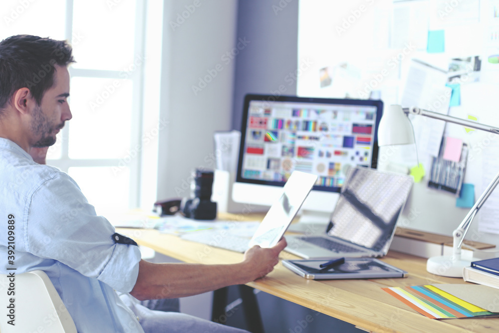 Poster portrait of young designer sitting at graphic studio in front of laptop and computer while working o