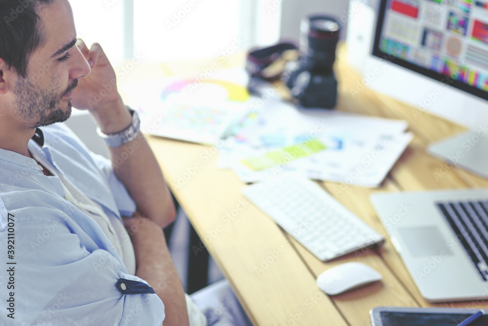 Poster portrait of young designer sitting at graphic studio in front of laptop and computer while working o